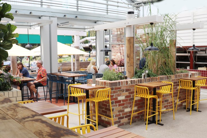 Outdoor cafe with colorful seating and brick planters, people dining.