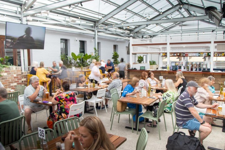 People dining at a bustling outdoor restaurant with a glass roof.