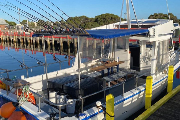 Fishing boat docked at a marina with multiple fishing rods secured and orange buoys attached.