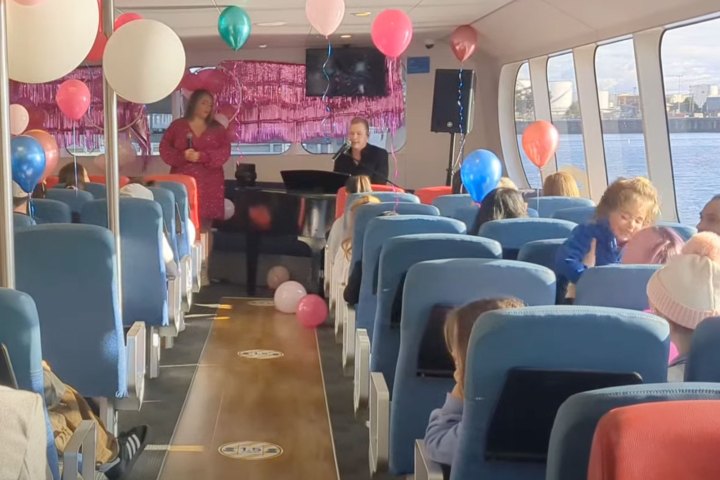 Interior of a party boat with pink and blue balloons, people seated, and live music performance.