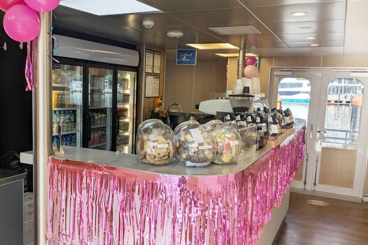 Cafe counter with pink decorations, snacks in jars, fridge with drinks, and pink balloons.