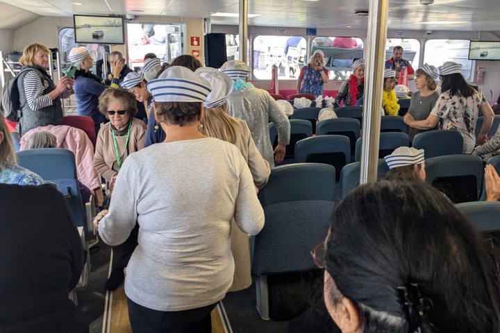 Group of people wearing striped sailor hats inside a boat's seating area.