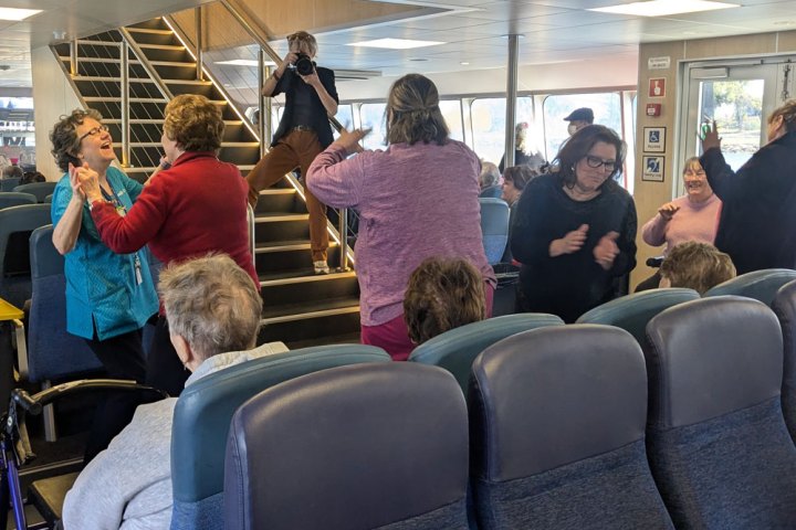 Group of people dancing and socializing inside a ferry with seating area.