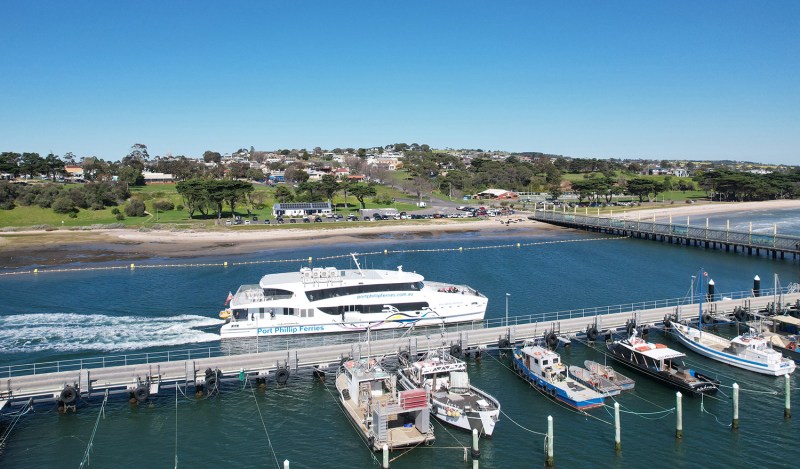 Aerial view of ferry and boats at a dock with a coastal town in the background.