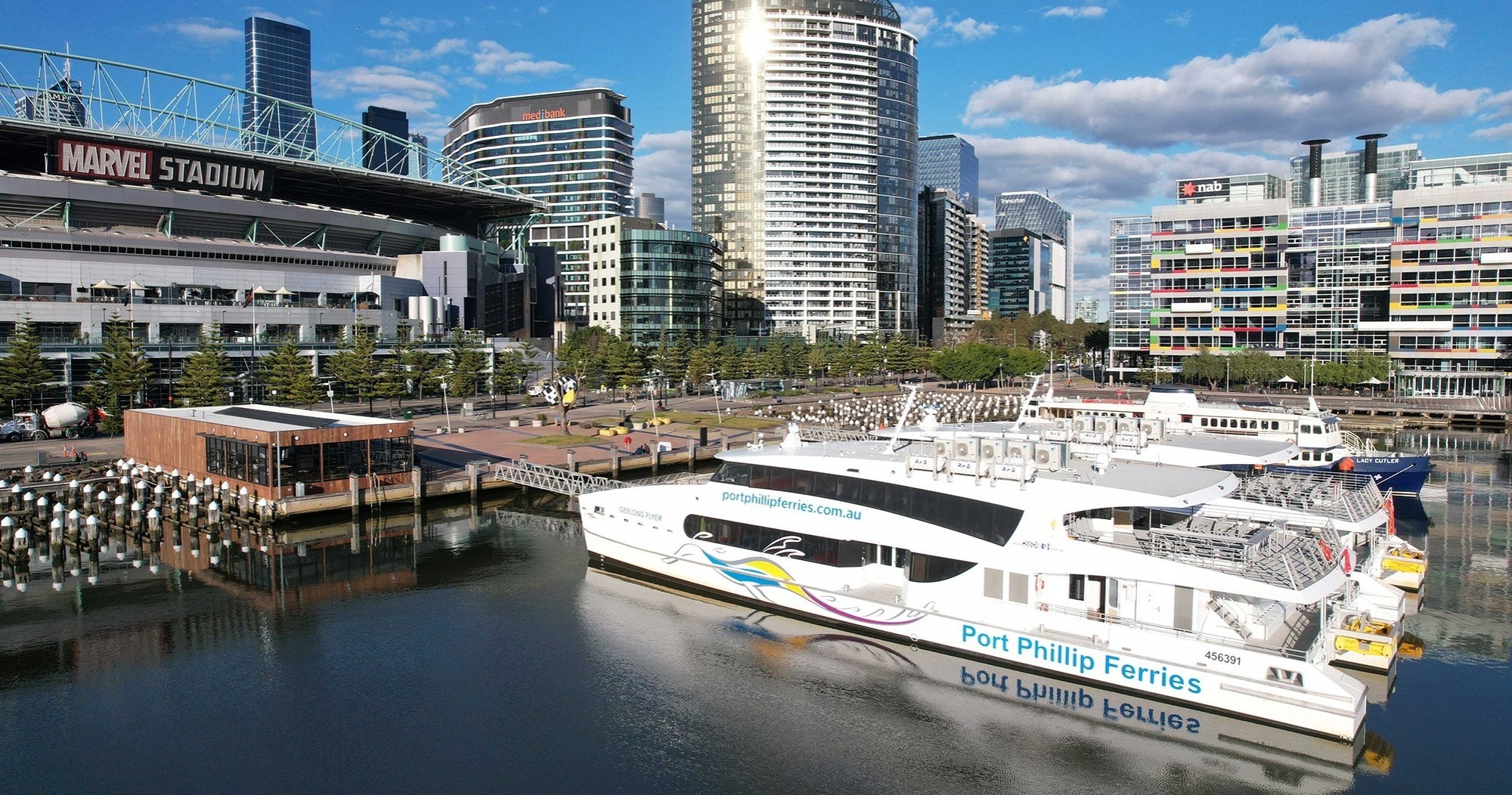 Ferry docked near stadium and modern buildings by a waterfront.