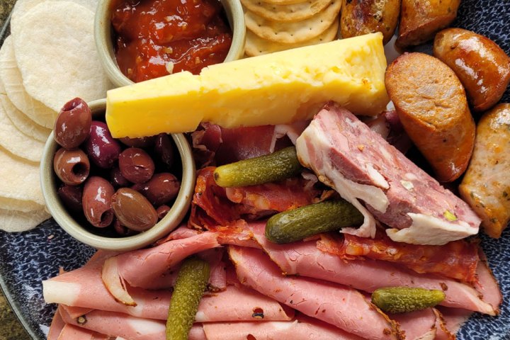 Charcuterie platter with meats, cheese, olives, pickles, crackers, and dip.