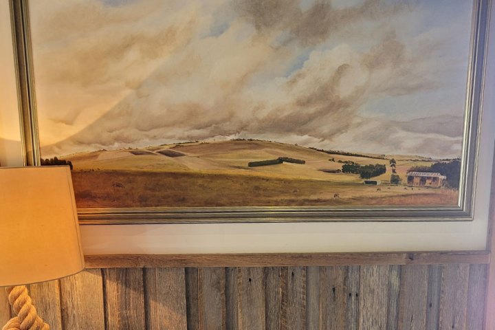 Framed landscape painting of a countryside with a cloudy sky above.