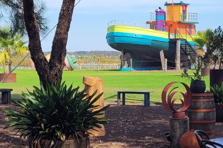 Colorful boat-shaped playground on lawn, surrounded by trees and benches.