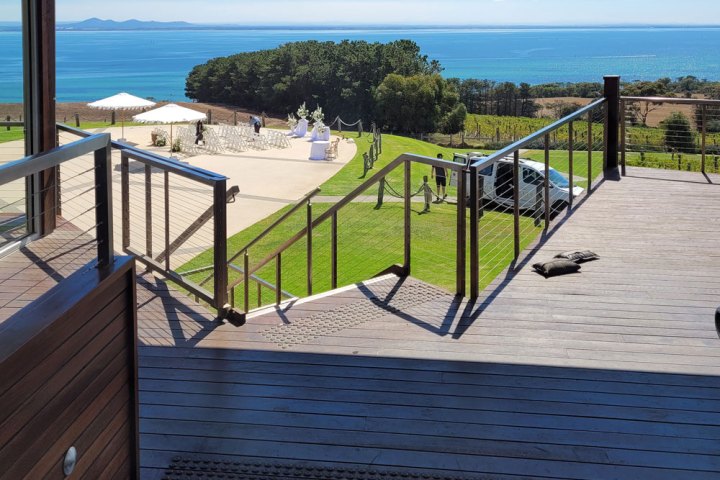 Deck view of grassy lawn, ocean, and distant hills under a clear sky.