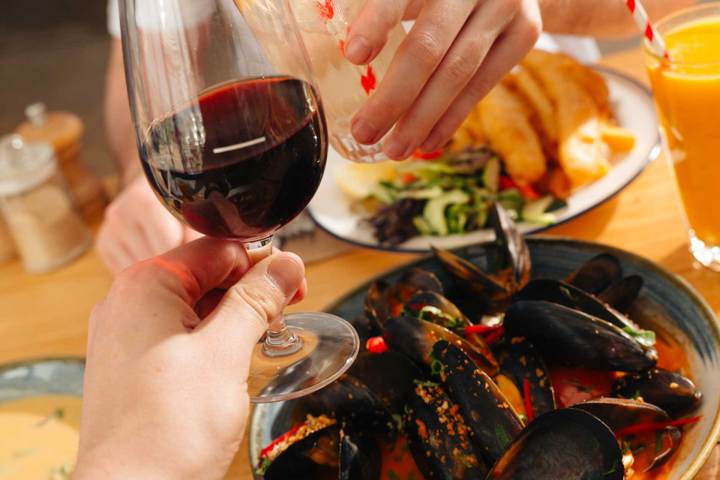Hands clinking wine glasses over a table with mussels and salad.