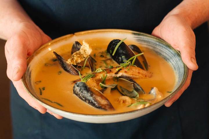 Hands holding a plate of creamy seafood soup with mussels and herbs.