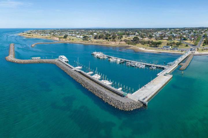 Aerial view of a coastal marina with boats docked and surrounding land.