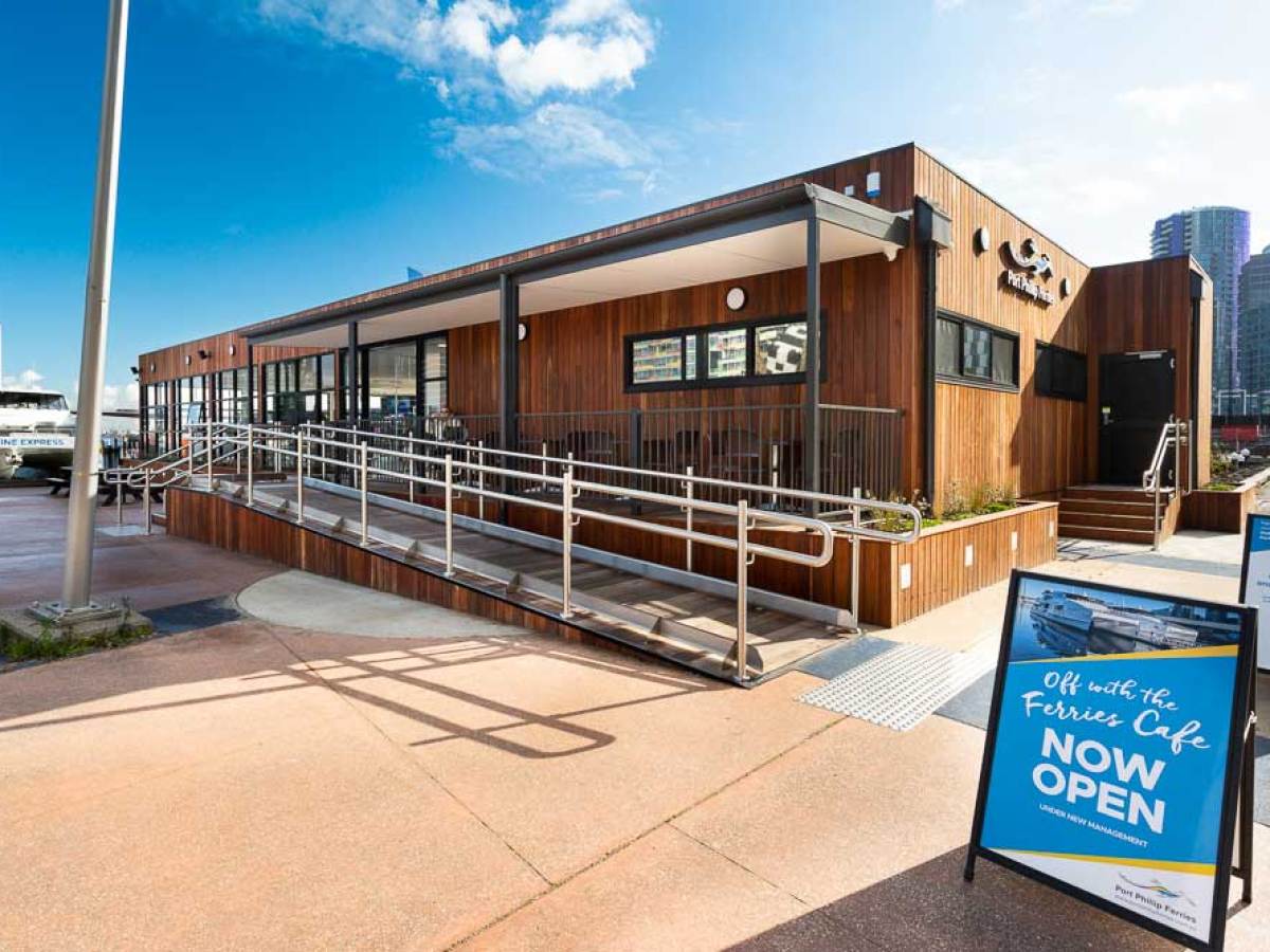 Wooden cafe building with a ramp and 'Now Open' sign outside.