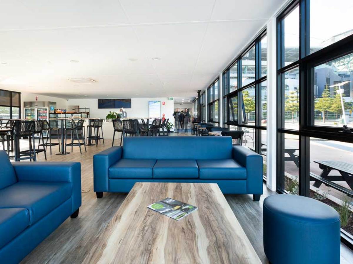 Modern lounge with blue sofas, wooden table, large windows, and outdoor view.