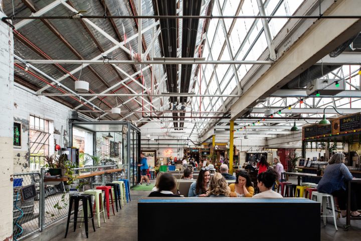 People dining in an industrial-style indoor food market with colorful seating.