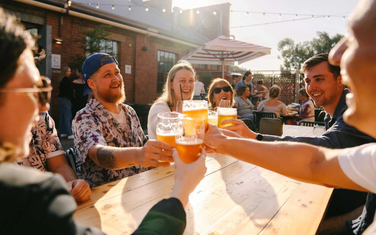 Group of people outdoors clinking glasses of beer at a wooden table.