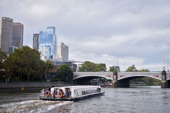 Boat on river with cityscape and bridge in the background.