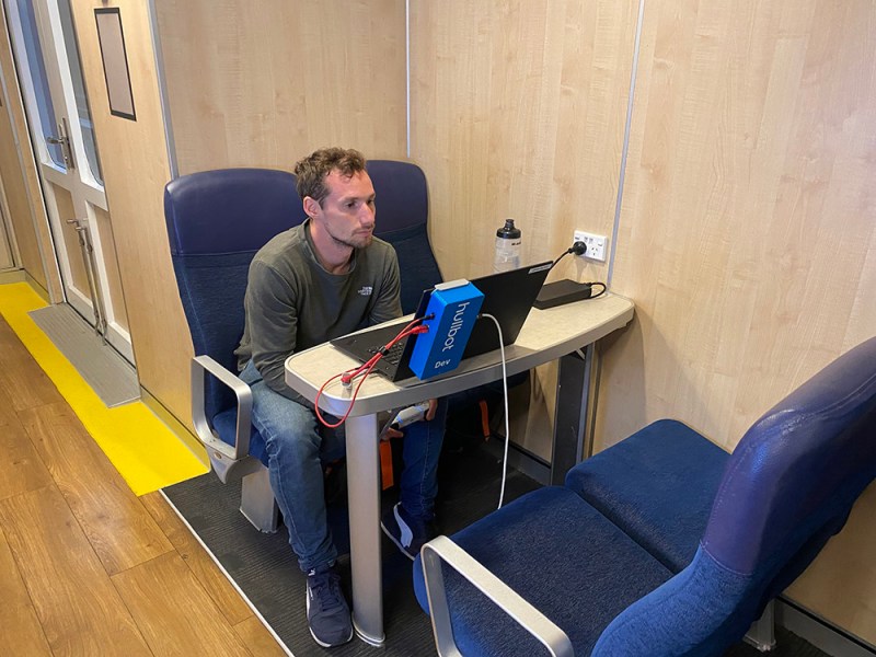 Person using a laptop with a small device attached on a train.