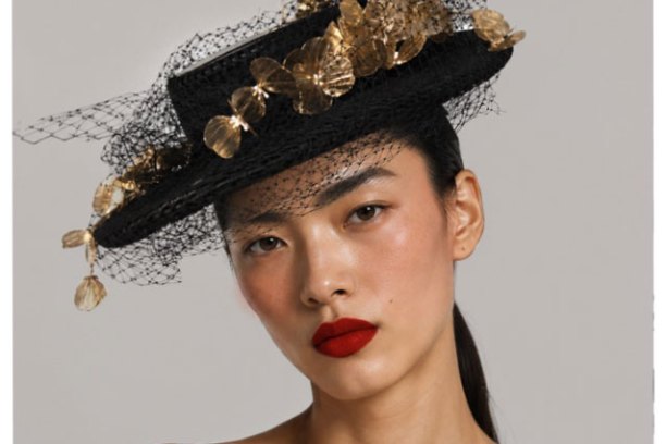 Woman with red lipstick wearing black hat with gold accents and netting.