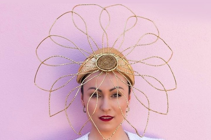 Person wearing elaborate gold wire headdress against pink wall.