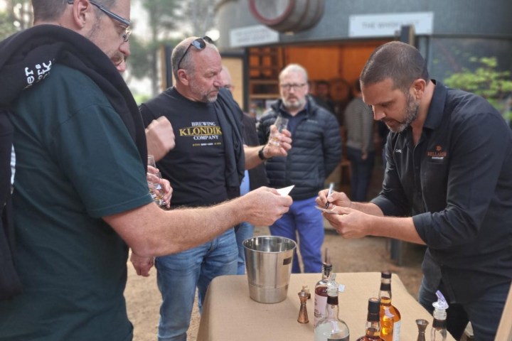 People tasting and discussing whiskey at an outdoor event.